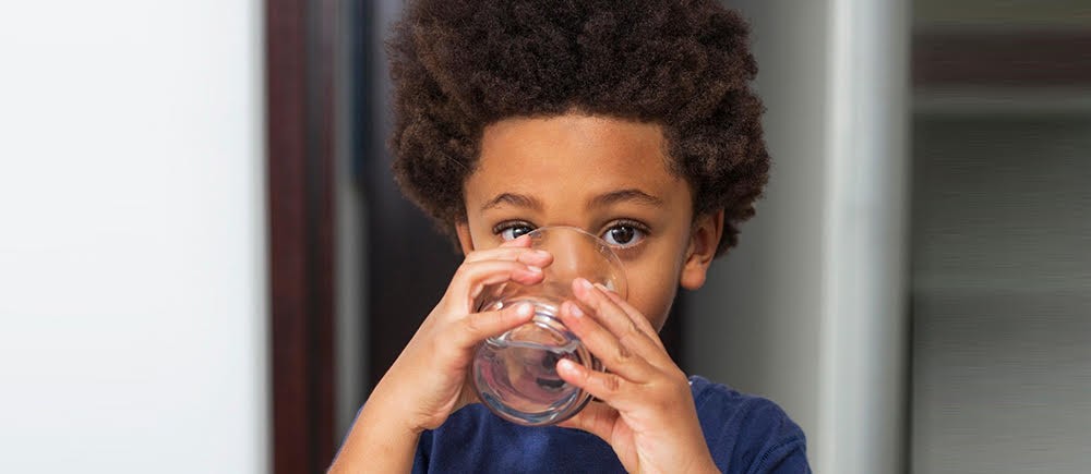 A young boy drinking from a glass of water. 