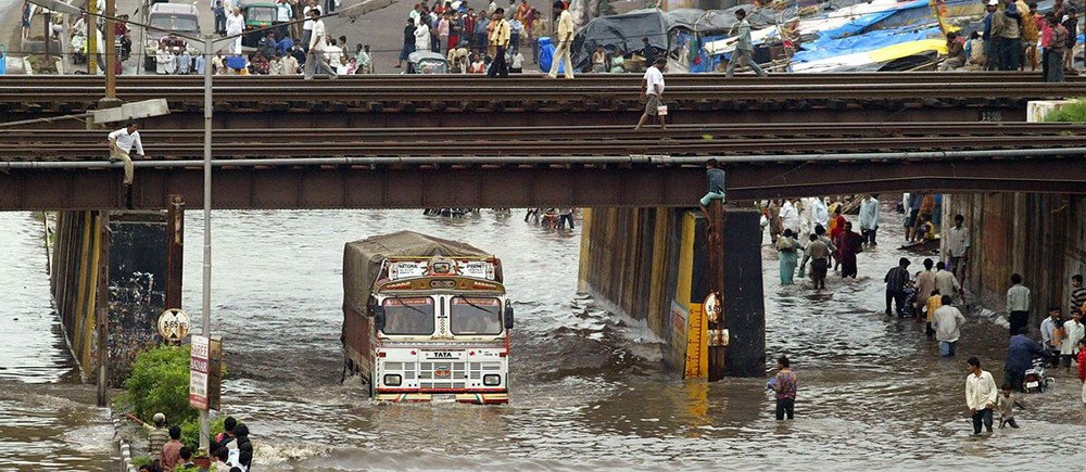 A bus being driven through a heavily flooded city.