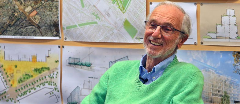 Architect Renzo Piano: Man with gray hair and beard with glasses wearing a lime green sweater and blue collared shirt sitting in front of maps and architectural drawings.