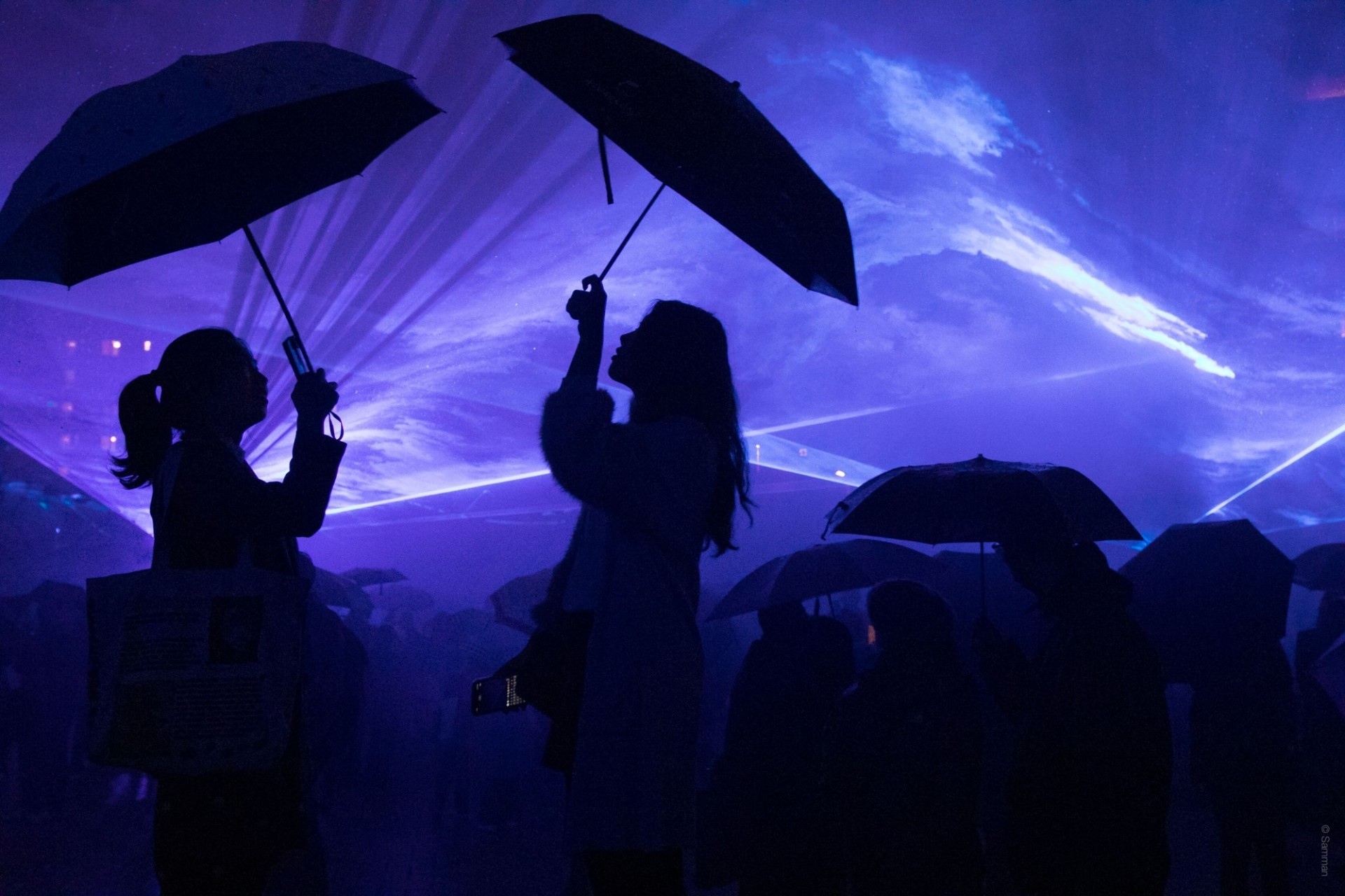 People in silhouette with umbrellas against a blue background of light