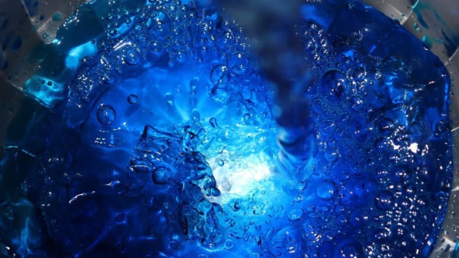 Photograph of water splashing in a container. Colors are shades of blue with bubbles and white light in the center.