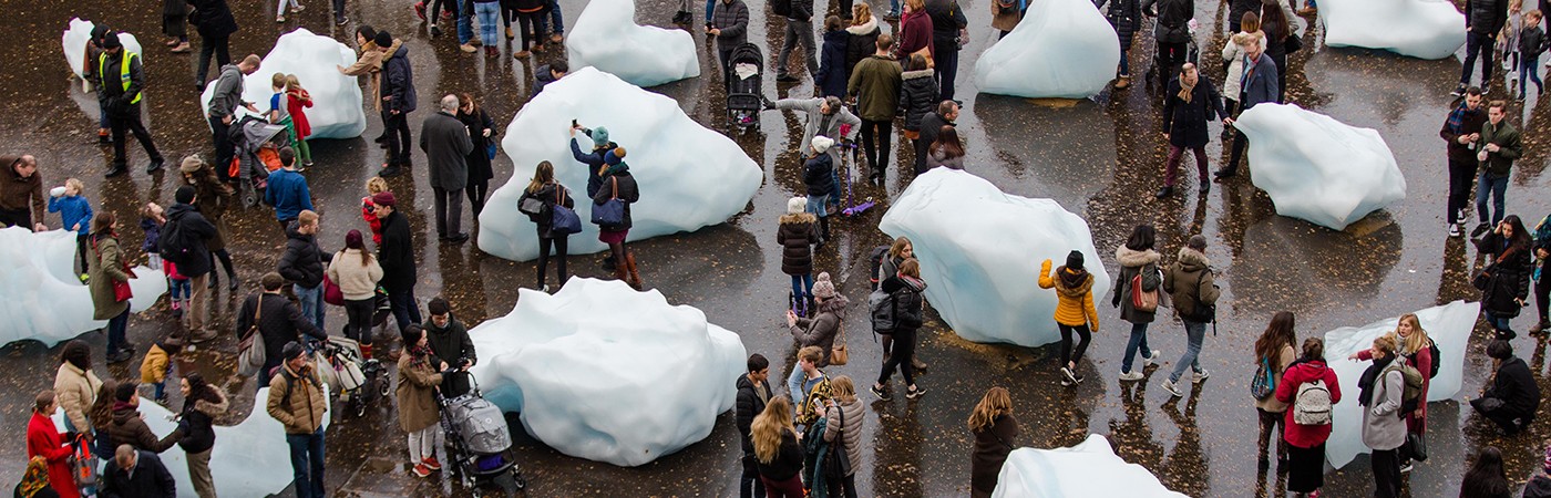 Dozens of people stroll through a plaza covered in very large blobs of ice.