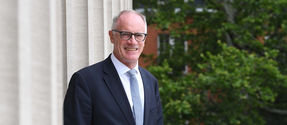 Dr. Alex N. Halliday, director of the Earth Institute: Man with gray hair and glasses in a suit and tie standing next to a column with a tree in the background.